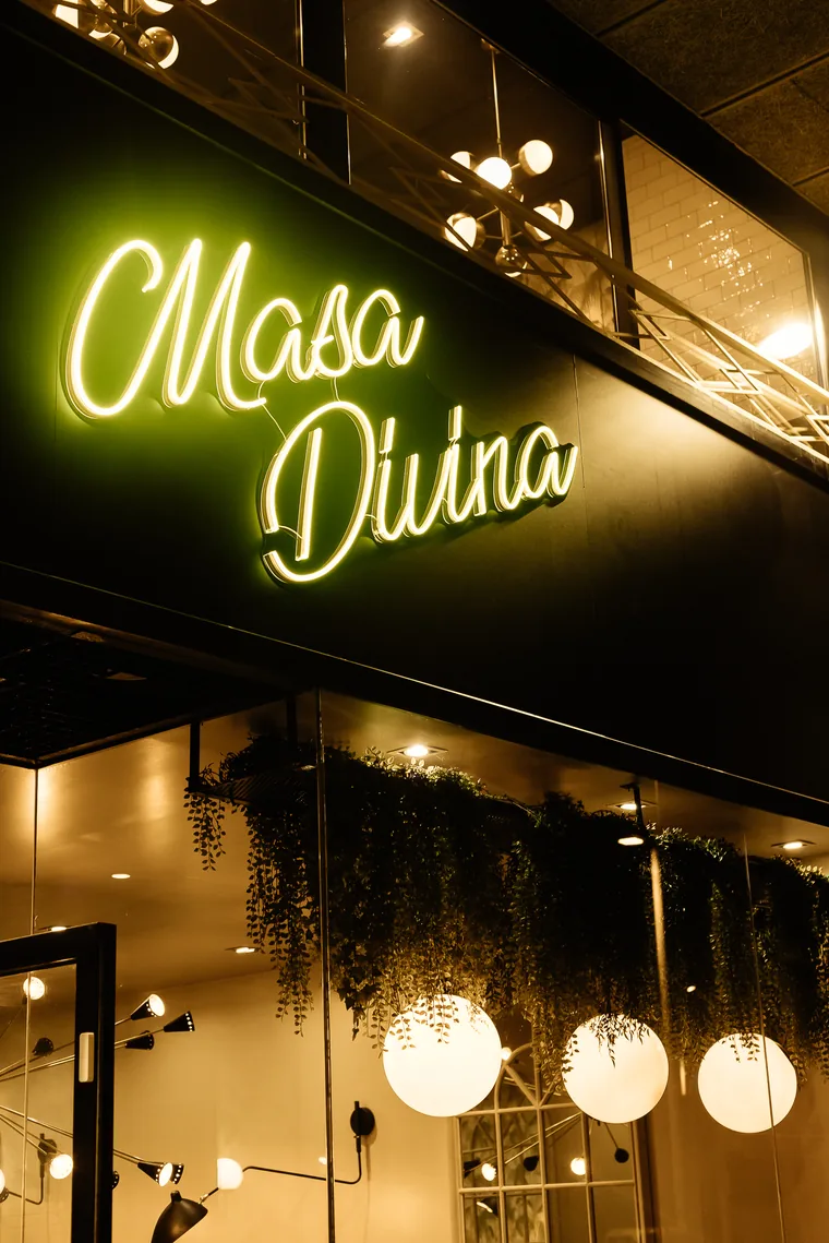 Fachada de Masa Divina de noche con el rótulo de neón encendido
