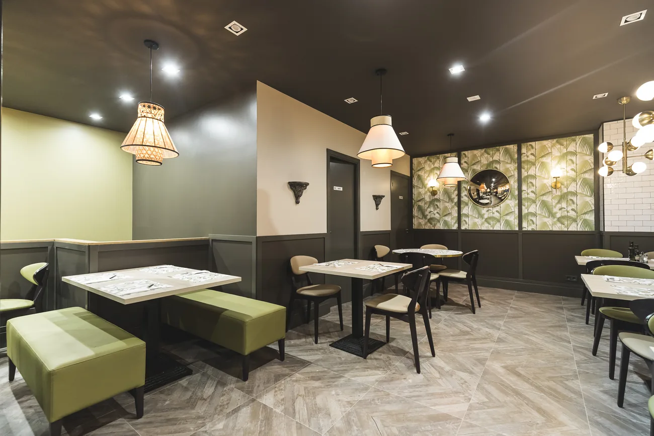 Comedor de Masa Divina con papel pintado de palmeras, lámparas de latón y banquetas verdes
